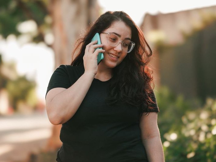 Smiling woman with curly hair and glasses talking on her smartphone outdoors